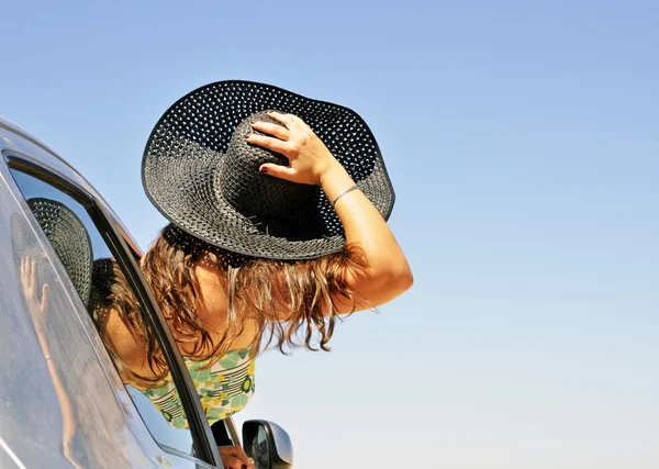 Mujer sosteniendo el sombrero asomándose por la ventana del coche. Imagen que representa fre — Foto de Stock