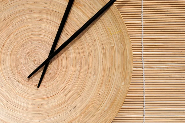Palillos japoneses en plato redondo de madera sobre fondo mantel de bambú — Foto de Stock