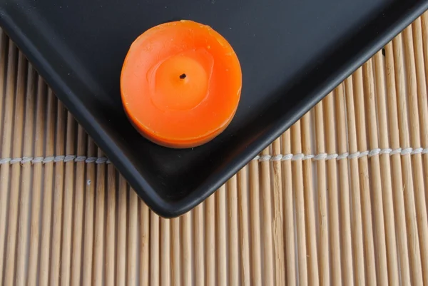 Oranje kaars in zwarte schotel op bamboe — Stockfoto