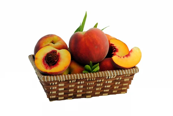 Целые и нарезанные персики в соломенной корзине — стоковое фото