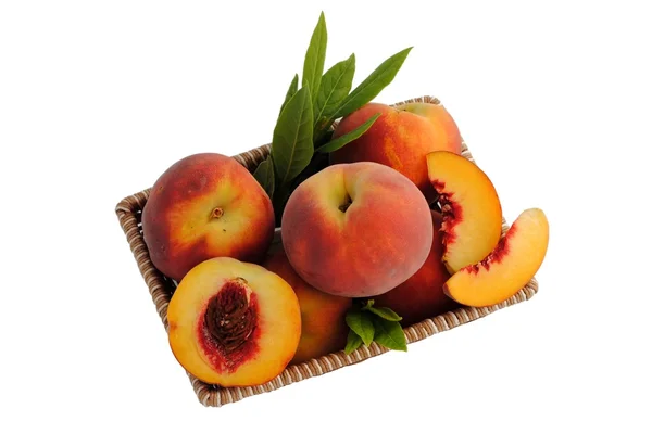 Whole and sliced peaches in a straw basket — Stock Photo, Image