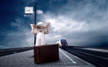 Little girl sitting on vintage baggage on the train platform of clipart