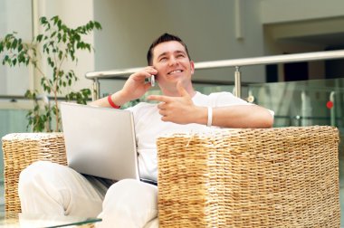 Smiling young man working on laptop computer and call by phone a clipart