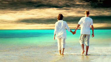 Rear view of a couple walking on the beach, holding hands. clipart