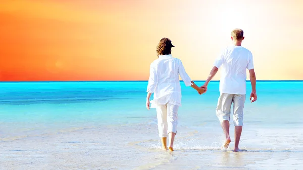 Bakifrån av ett par promenader på stranden, hålla händerna. — Stockfoto