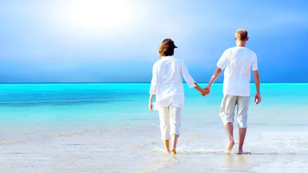 Bakifrån av ett par promenader på stranden, hålla händerna. — Stockfoto