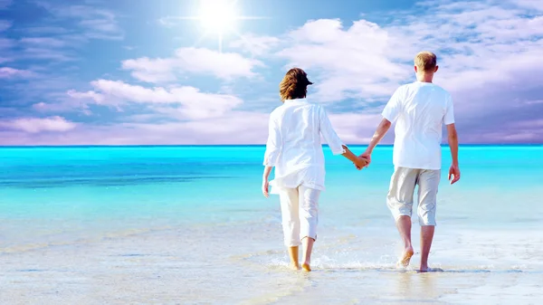 Вид сзади на пару, идущую по пляжу, держащихся за руки. — стоковое фото