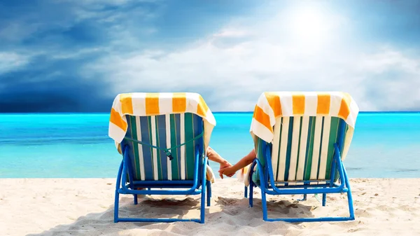 Vista posteriore di una coppia su una sedia a sdraio per rilassarsi sulla spiaggia — Foto Stock