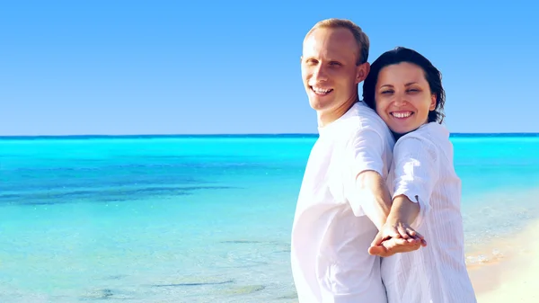 Вид счастливой молодой пары, идущей по пляжу, держась за руки . — стоковое фото