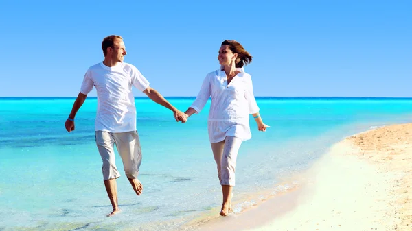 Visa lyckliga unga paret promenerar på stranden, hand i hand. — Stockfoto