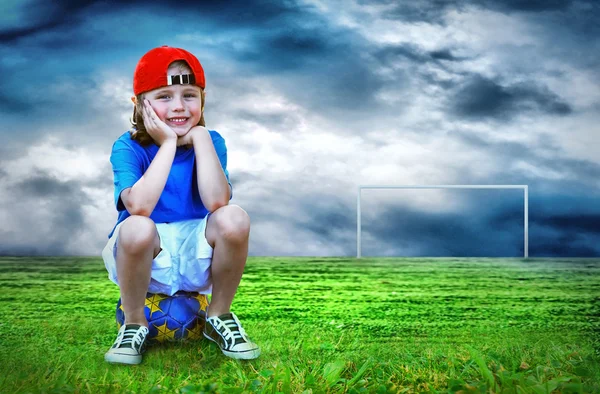 Young boy seating on the ball in green field — Stock Photo, Image