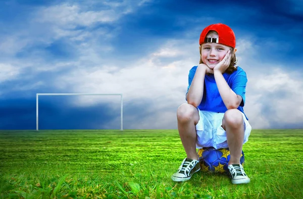 Young boy seating on the ball in green field — Stock Photo, Image