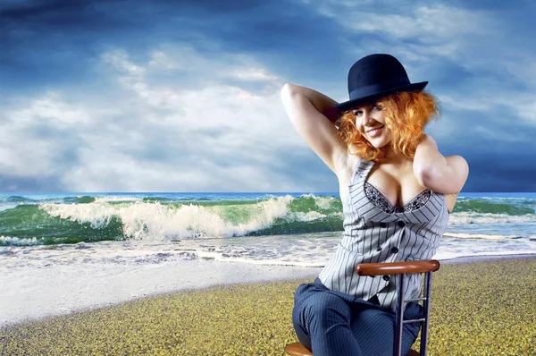 Молода жінка в чорному капелюсі сидить на пляжі — стокове фото