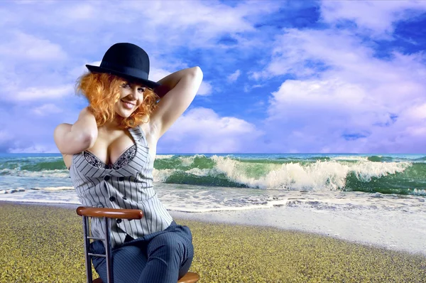 Mladá žena v černém klobouku posezením na pláži — Stock fotografie