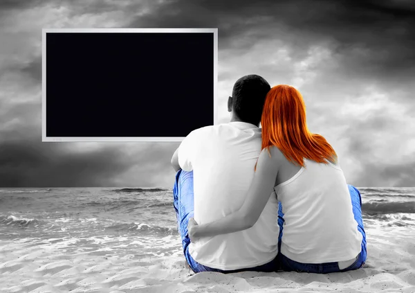 Havsutsikt över ett par sitter på stranden och se TV-monitor — Stockfoto