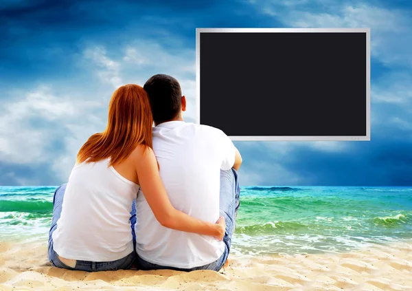 Meerblick eines Paares, das am Strand sitzt und den Fernseher ansieht — Stockfoto