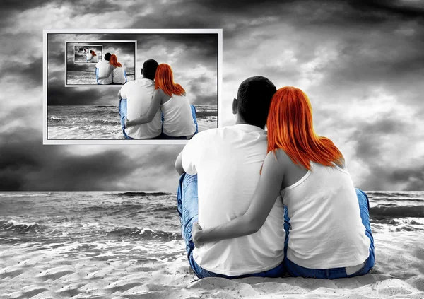 Zeezicht van een paar zittend op het strand en zie tv-monitor — Stockfoto