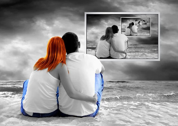 Вид на море пара, сидящая на пляже и смотреть телевизор монитор — стоковое фото