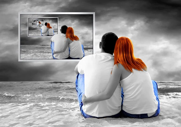 Havsutsikt över ett par sitter på stranden och se TV-monitor — Stockfoto