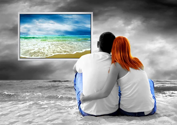 Zeezicht van een paar zittend op het strand en zie tv-monitor — Stockfoto
