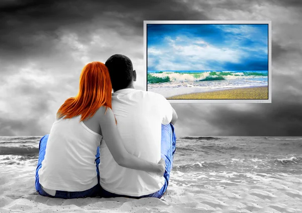 Vista al mar de una pareja sentada en la playa y ver el monitor de TV — Foto de Stock