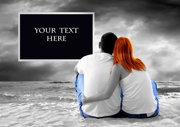 Vista al mar de una pareja sentada en la playa y ver el monitor de TV — Foto de Stock