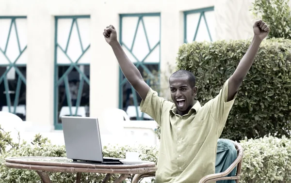 Jeune homme heureux ou étudiant avec ordinateur portable assis à la table — Photo