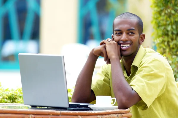 Joven hombre feliz o estudiante con portátil sentado a la mesa —  Fotos de Stock