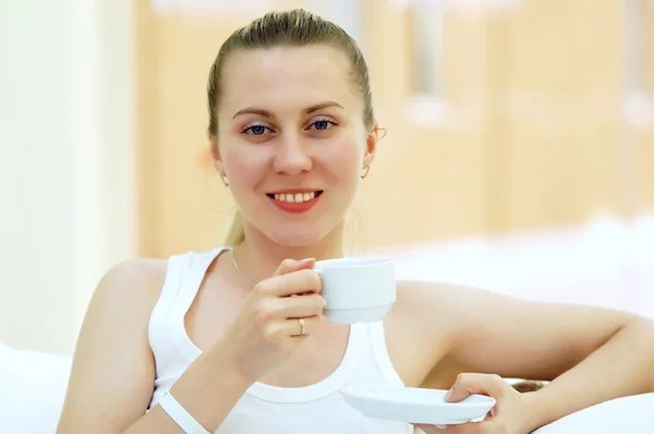 Mujer feliz en blanco con taza de café o té en el dormitorio — Foto de Stock