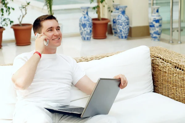 Sorridente giovane uomo che lavora sul computer portatile e chiamare per telefono un — Foto Stock