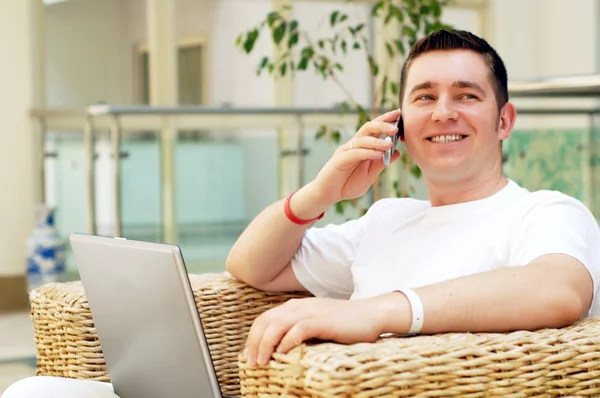 Leende unga mannen arbetar på bärbar dator och ringa på telefon en — Stockfoto