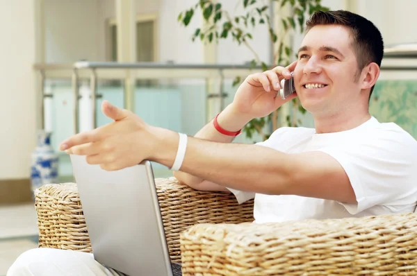 Smiling young man working on laptop computer and call by phone a — Stock Photo, Image