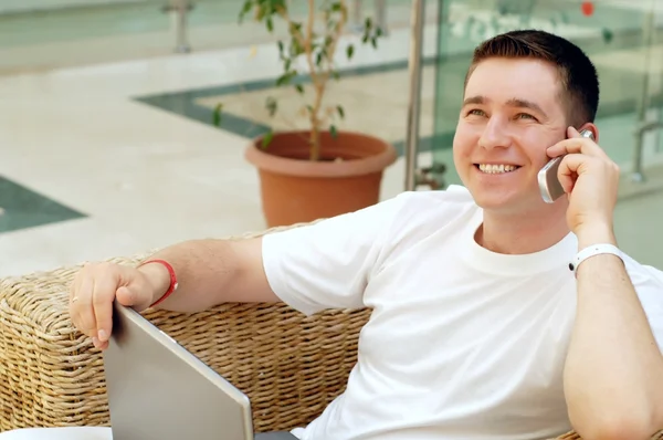 Smiling young man working on laptop computer and call by phone a — Stock Photo, Image