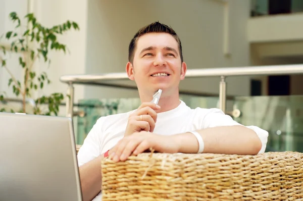 Genç gülümseyen adam dizüstü bilgisayar üzerinde çalışan ve telefonla ara bir — Stok fotoğraf