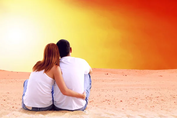 Молодая пара, сидящая в пустыне в солнечный день — стоковое фото