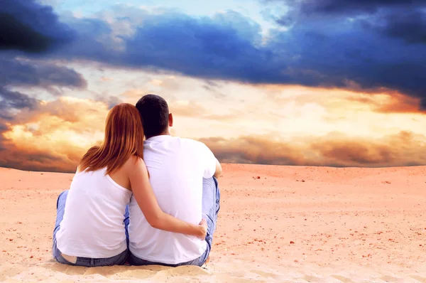 Молодая пара, сидящая в пустыне в солнечный день — стоковое фото