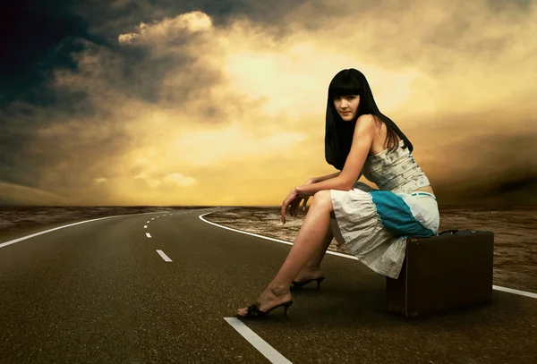 Молода жінка чекає на дорозі зі своїм старовинним багажем — стокове фото