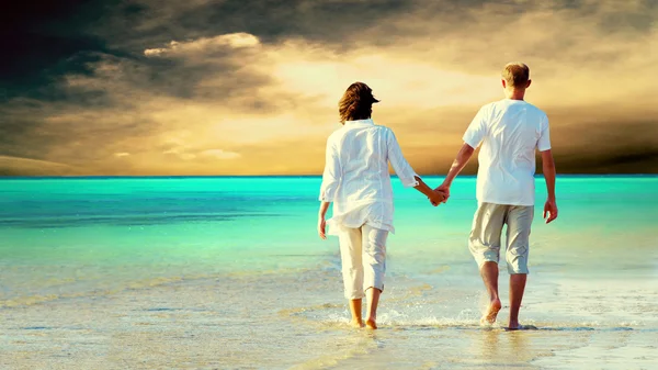 Вид сзади на пару, идущую по пляжу, держащихся за руки. — стоковое фото