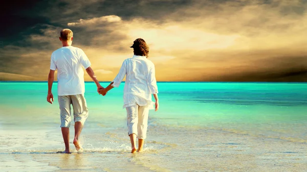 Rückansicht eines am Strand spazierenden Paares, das Händchen haltend. — Stockfoto