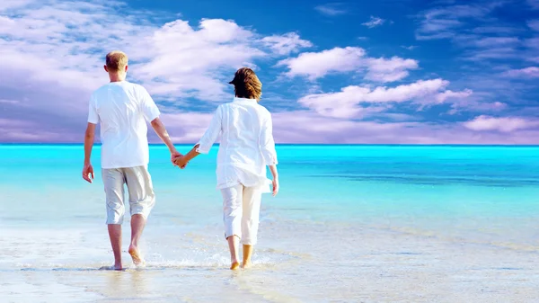 Rückansicht eines am Strand spazierenden Paares, das Händchen haltend. Stockbild