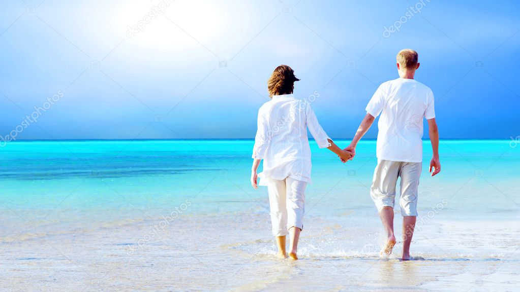 Rear view of a couple walking on the beach, holding hands.