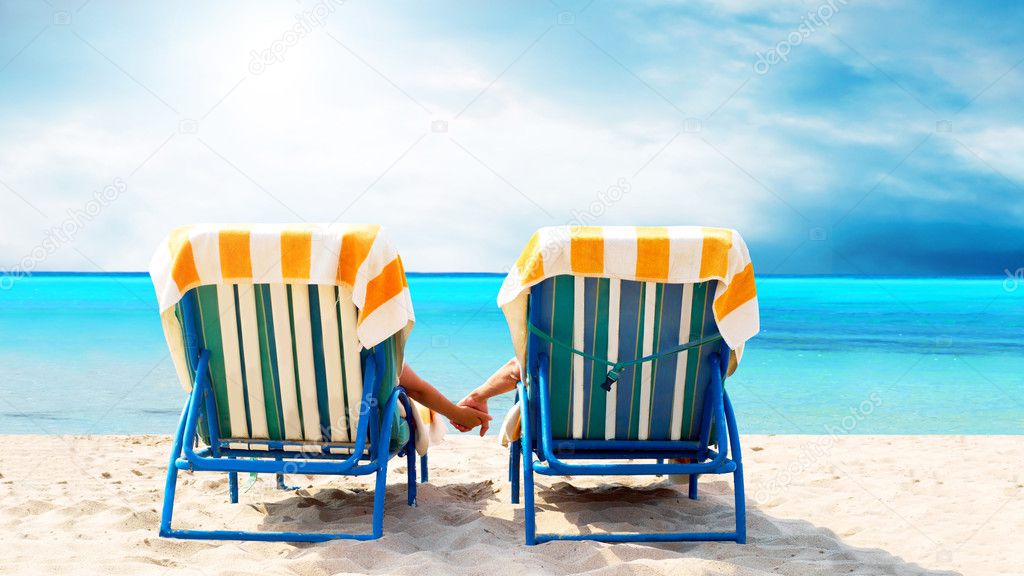 Rear view of a couple on a deck chair relaxing on the beach