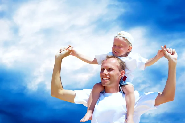 Joyful father giving piggyback ride to his son against a sky bac — Stock Photo, Image