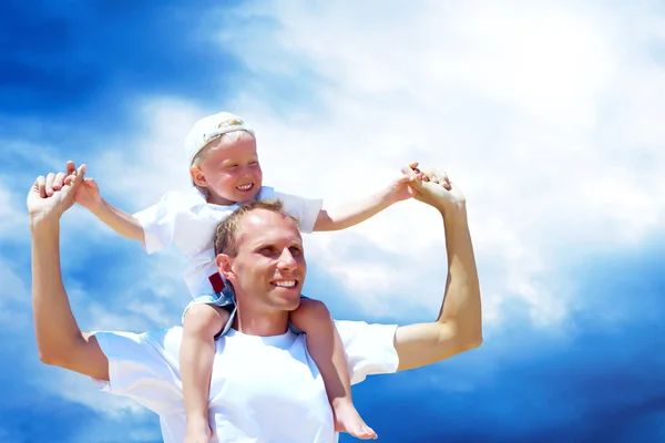 Vrolijke vader piggyback rit geven aan zijn zoon tegen een hemel bac — Stockfoto