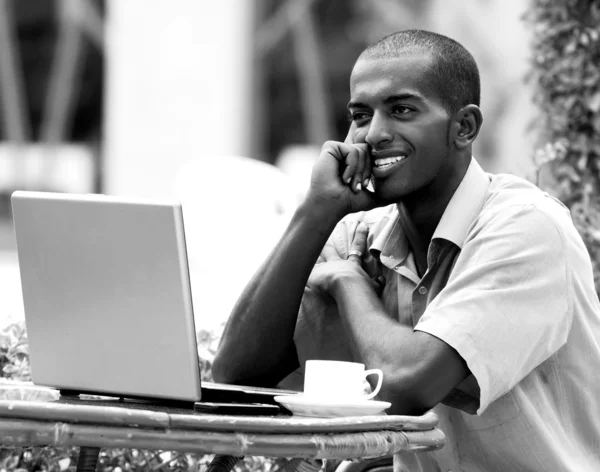 Joven hombre feliz o estudiante con portátil sentado a la mesa — Foto de Stock