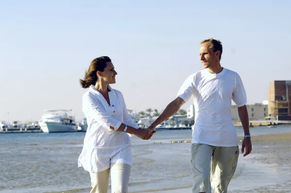Nézd, a boldog fiatal pár séta a tengerparton, kézenfogva. — Stock Fotó