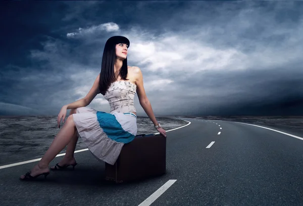 Молода жінка чекає на дорозі зі своїм старовинним багажем — стокове фото