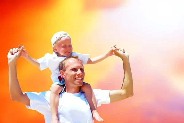 O pai alegre que dá o passeio do piggyback a seu filho contra um bac do céu — Fotografia de Stock