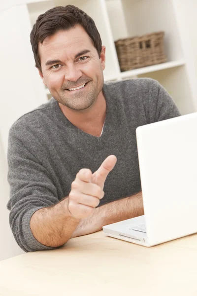 Uśmiechnięty mężczyzna w domu przy użyciu komputera przenośnego, wskazując na aparat — Zdjęcie stockowe