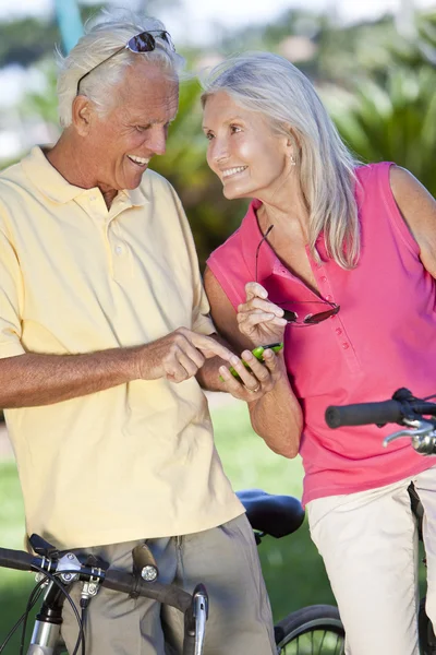 Feliz pareja de personas mayores en bicicleta usando el teléfono inteligente en Sunshin —  Fotos de Stock